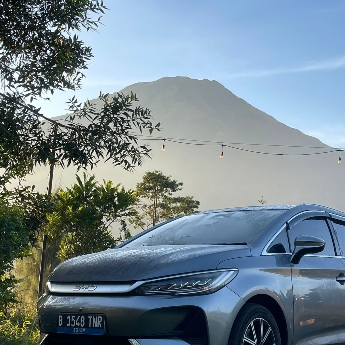 Mobil listrik dengan latar gunung dan lampu gantung di camp ground